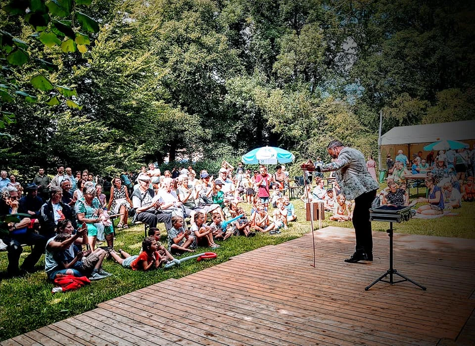 Publiek in het gras kijkt naar een openluchtvoorstelling van Armand Magic